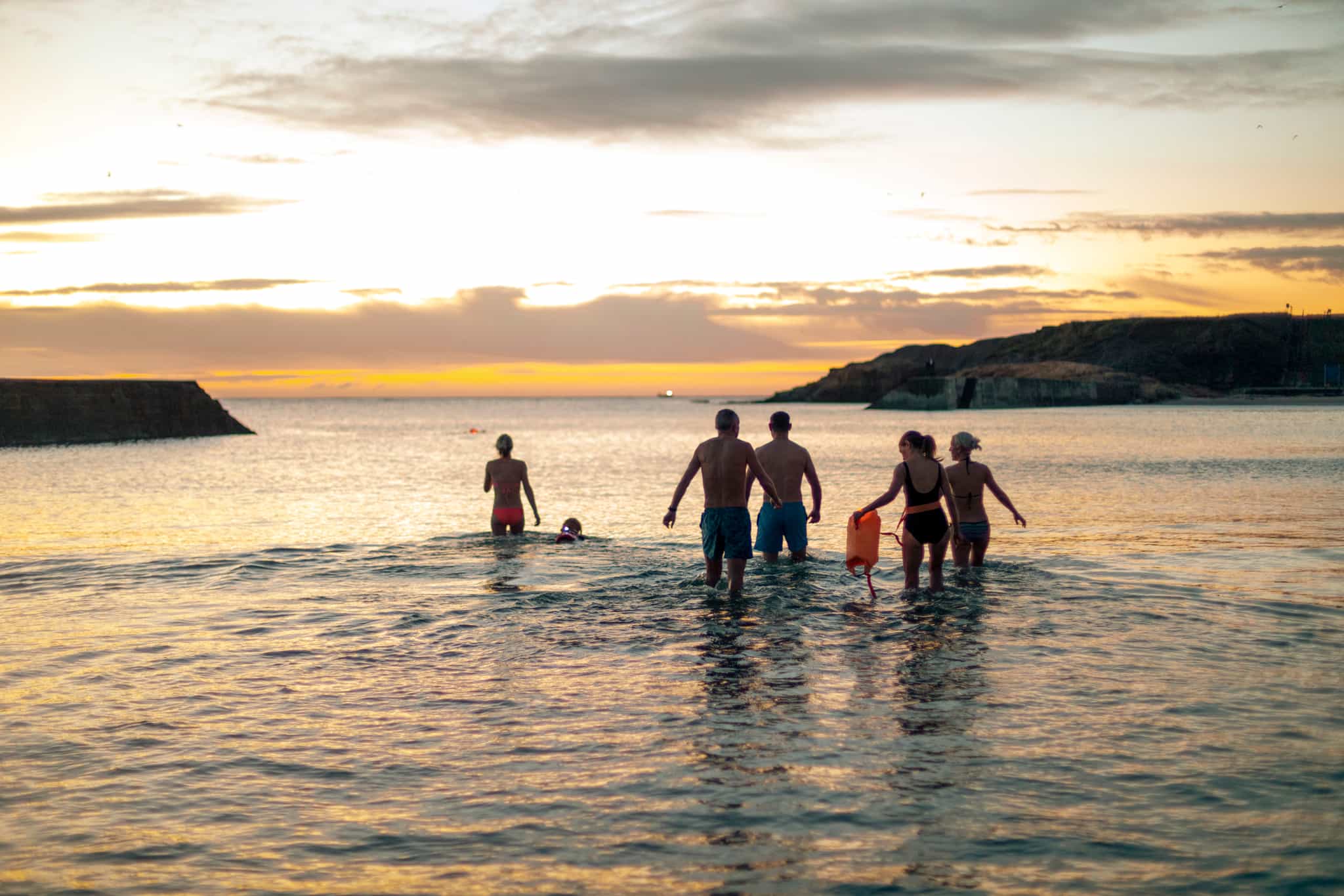 View of a group of friends walking out into the ocean while open water swimming at dawn, in the UK.