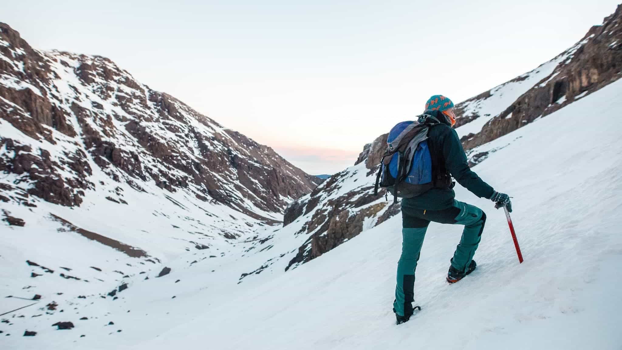 A mountain guide leans against his ice axe on the snowy slopes of Mount Toubkal, Morocco.