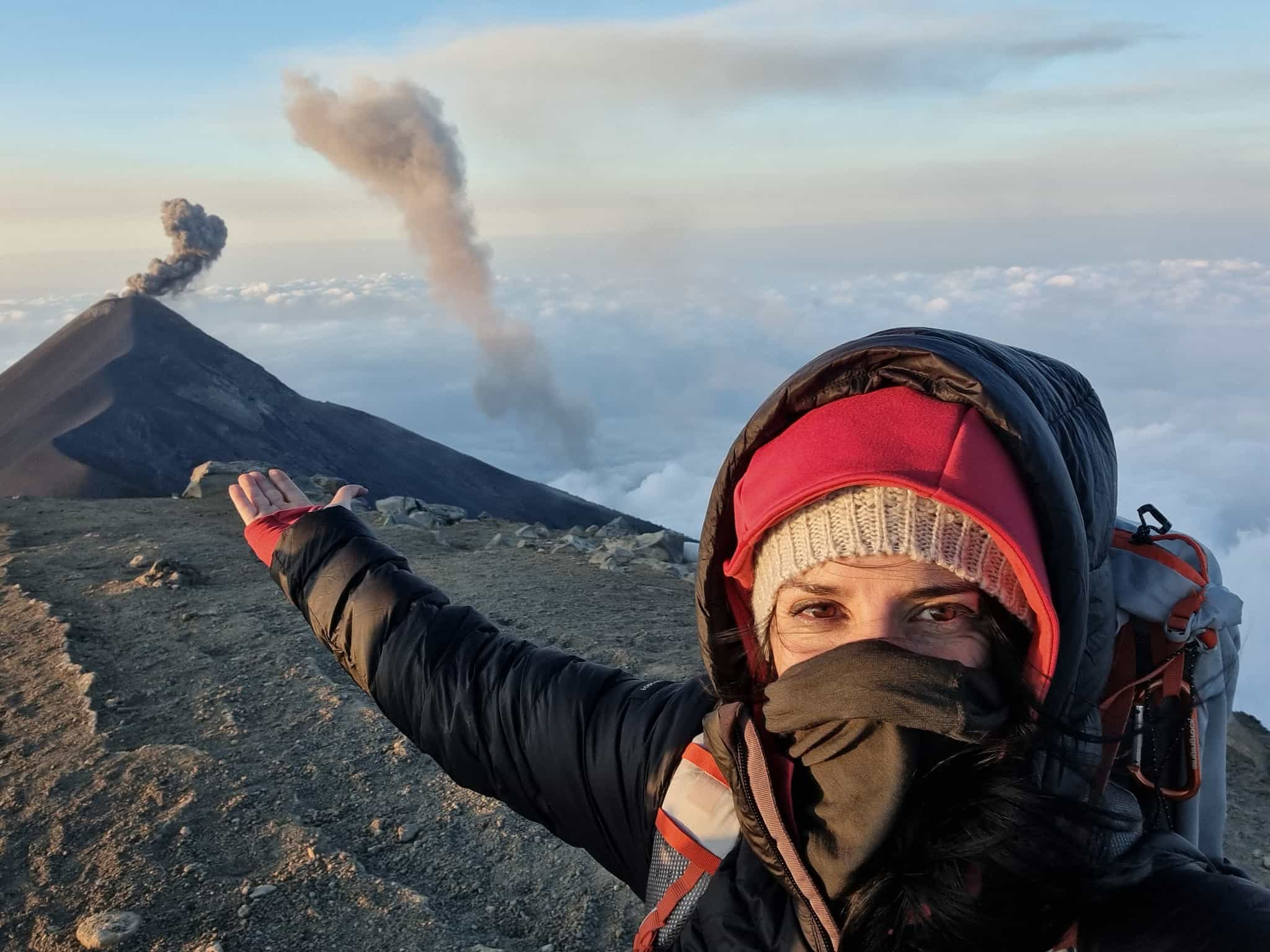 Female hiker at the summit of Acatenango volcano pointing towards the erupting Fuego volcano, Guatemala.
