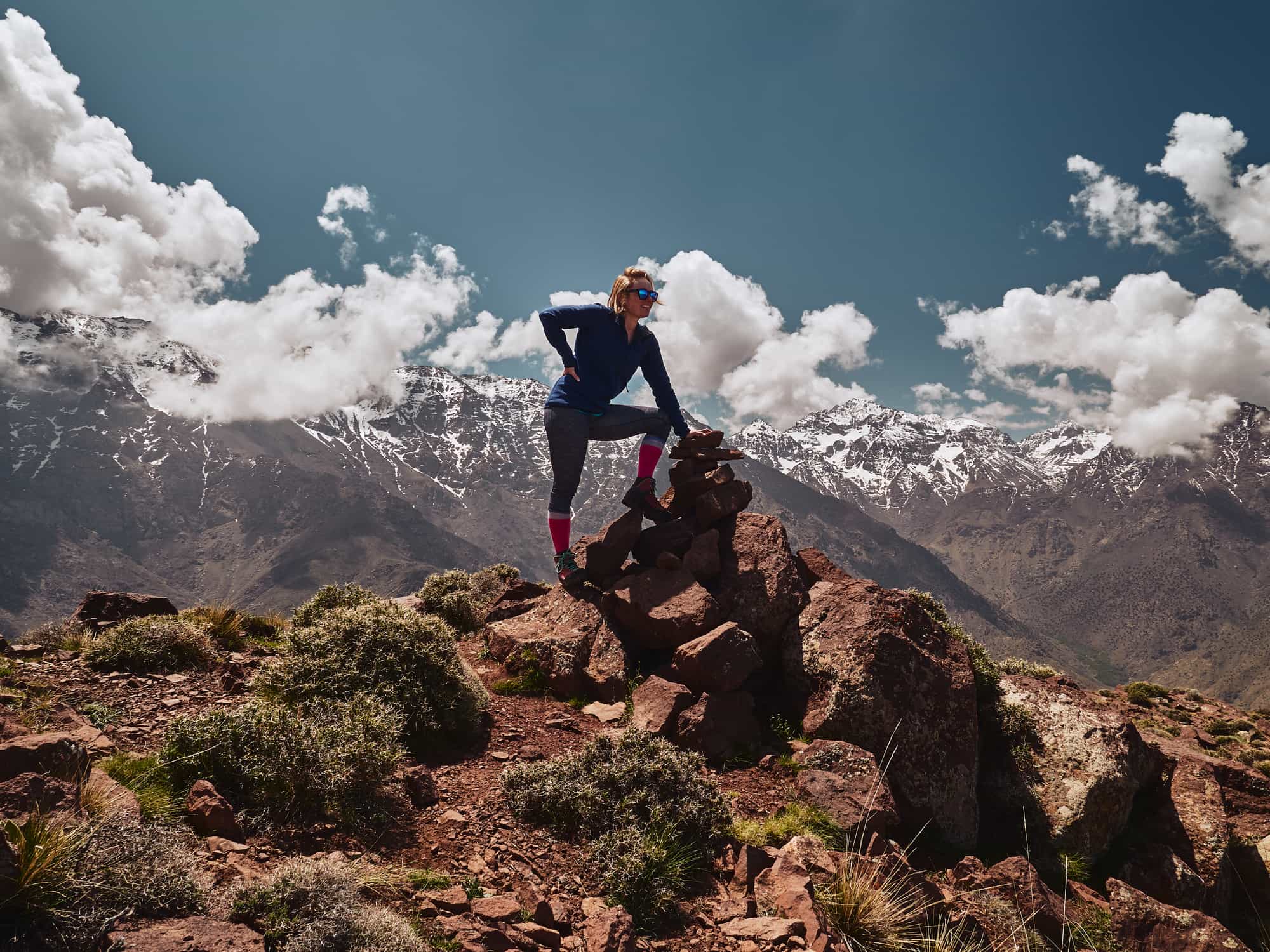 A woman leans against a rock on the rocky slopes of Mount Toubkal, Morocco.