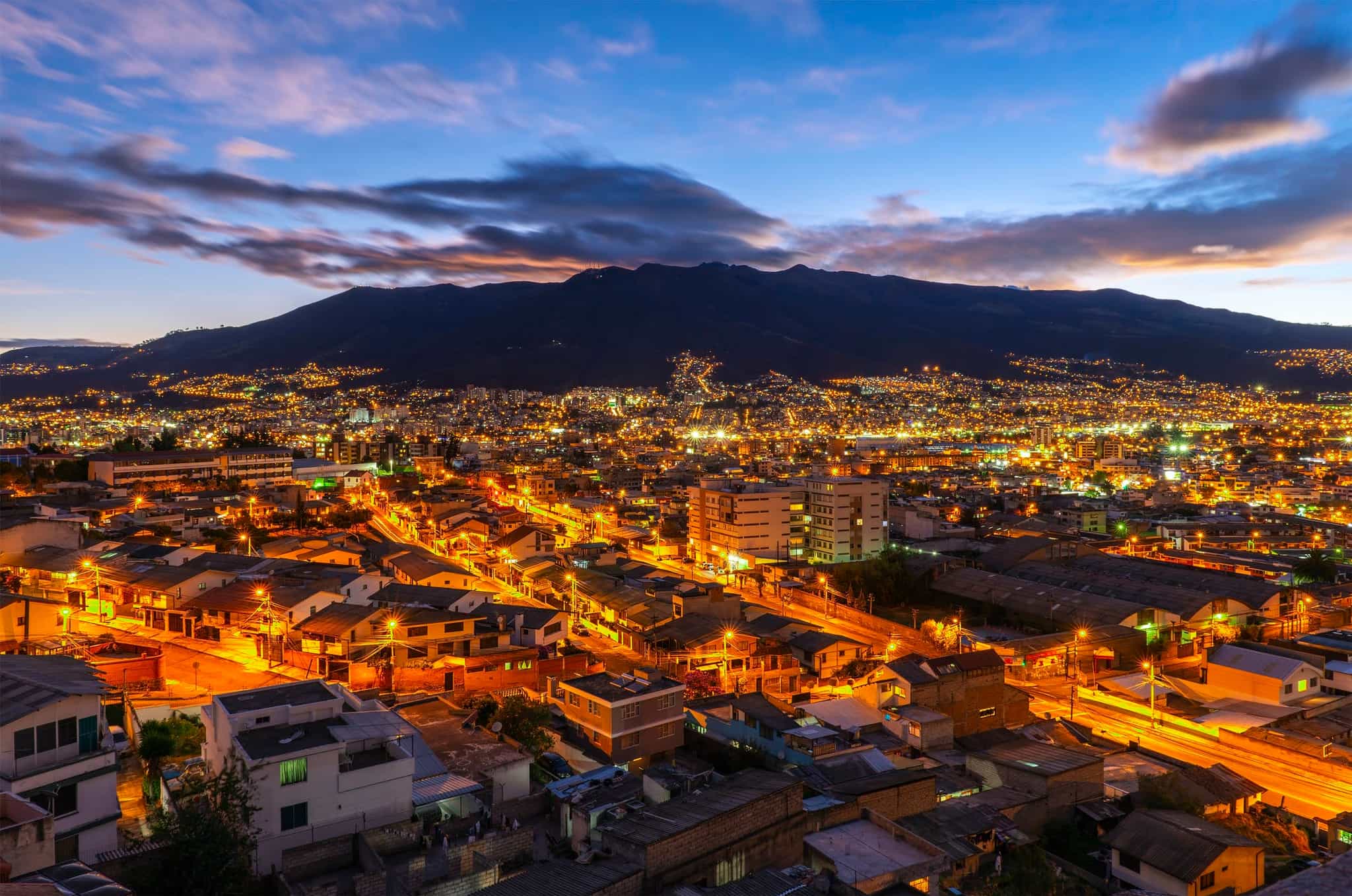 The skyline of Quito at sunset with city lights, backed by the Pichincha volcano, Ecuador.