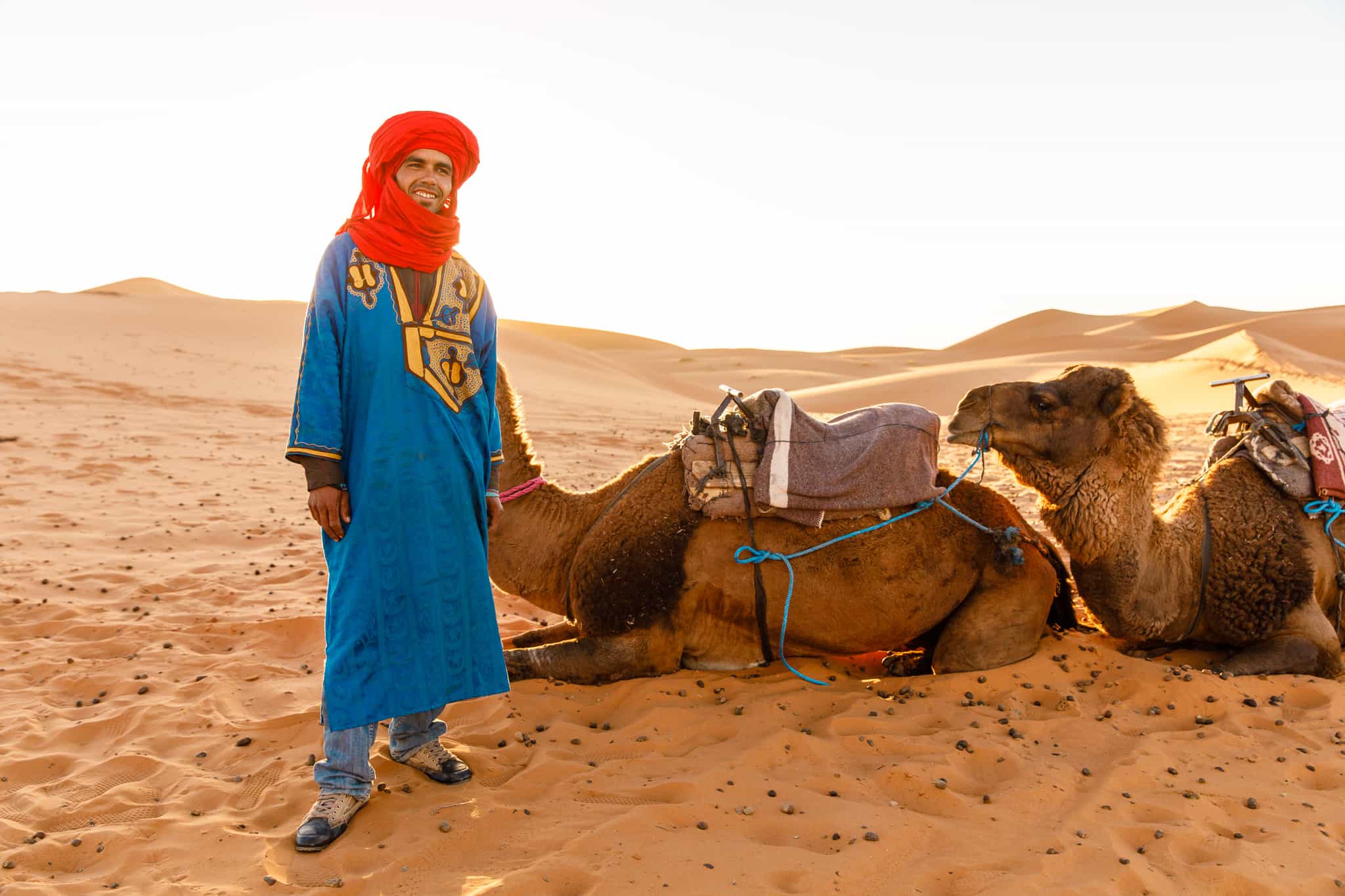 A Berber guide stands beside a camel in the Sahara Desert, Morocco.