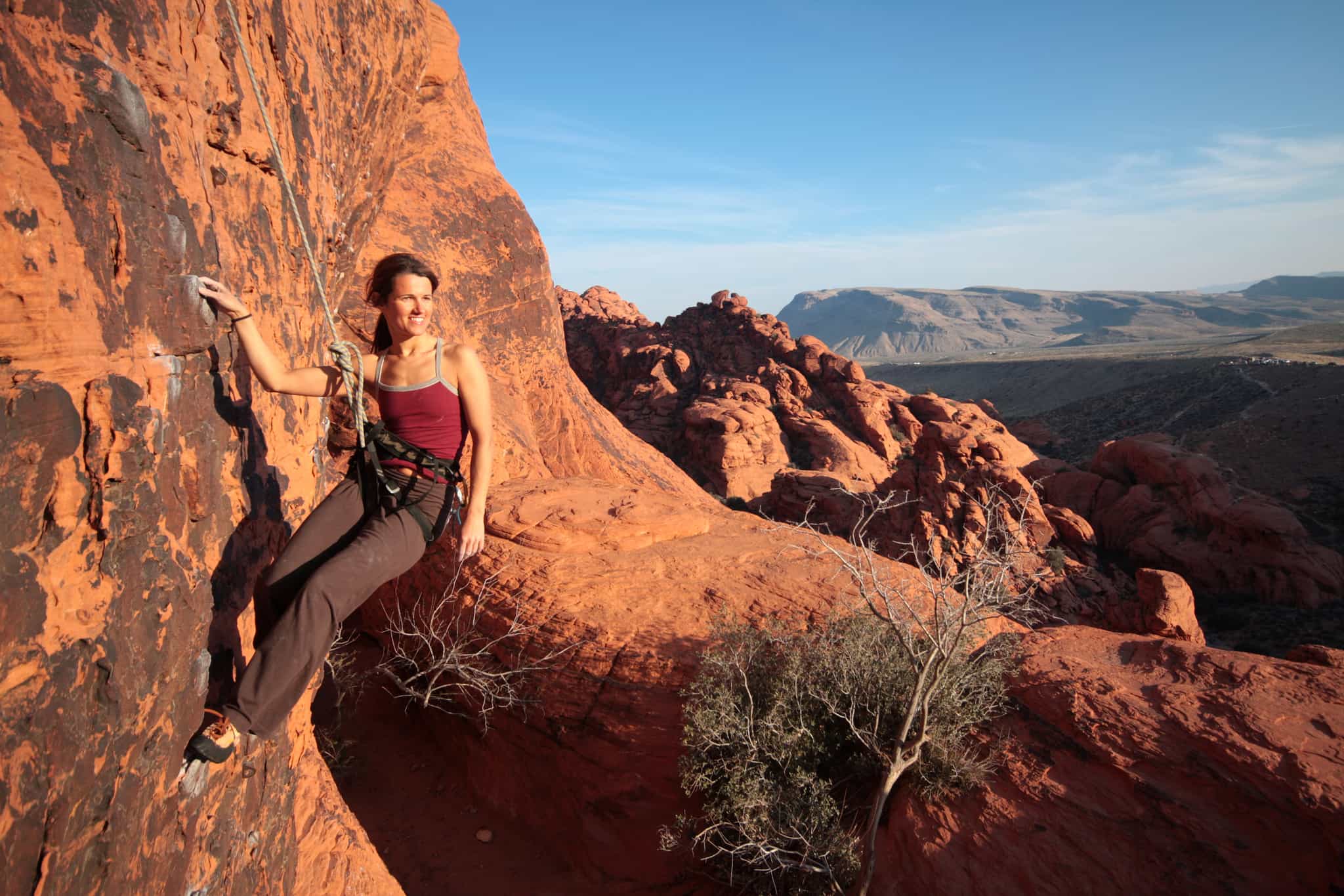 A female rock climber hangs from a rope on the red rock face of Morocco's Todra Gorge.
