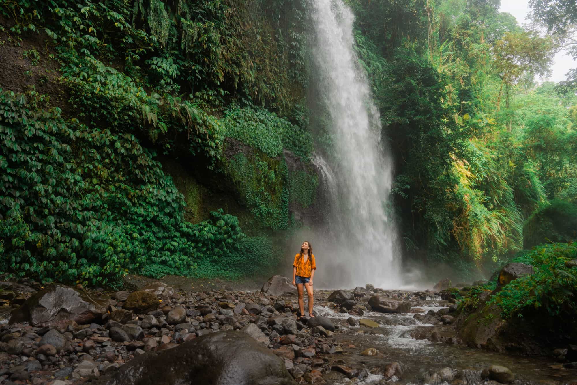Woman hiker passing by a waterfall in Bali, Indonesia.