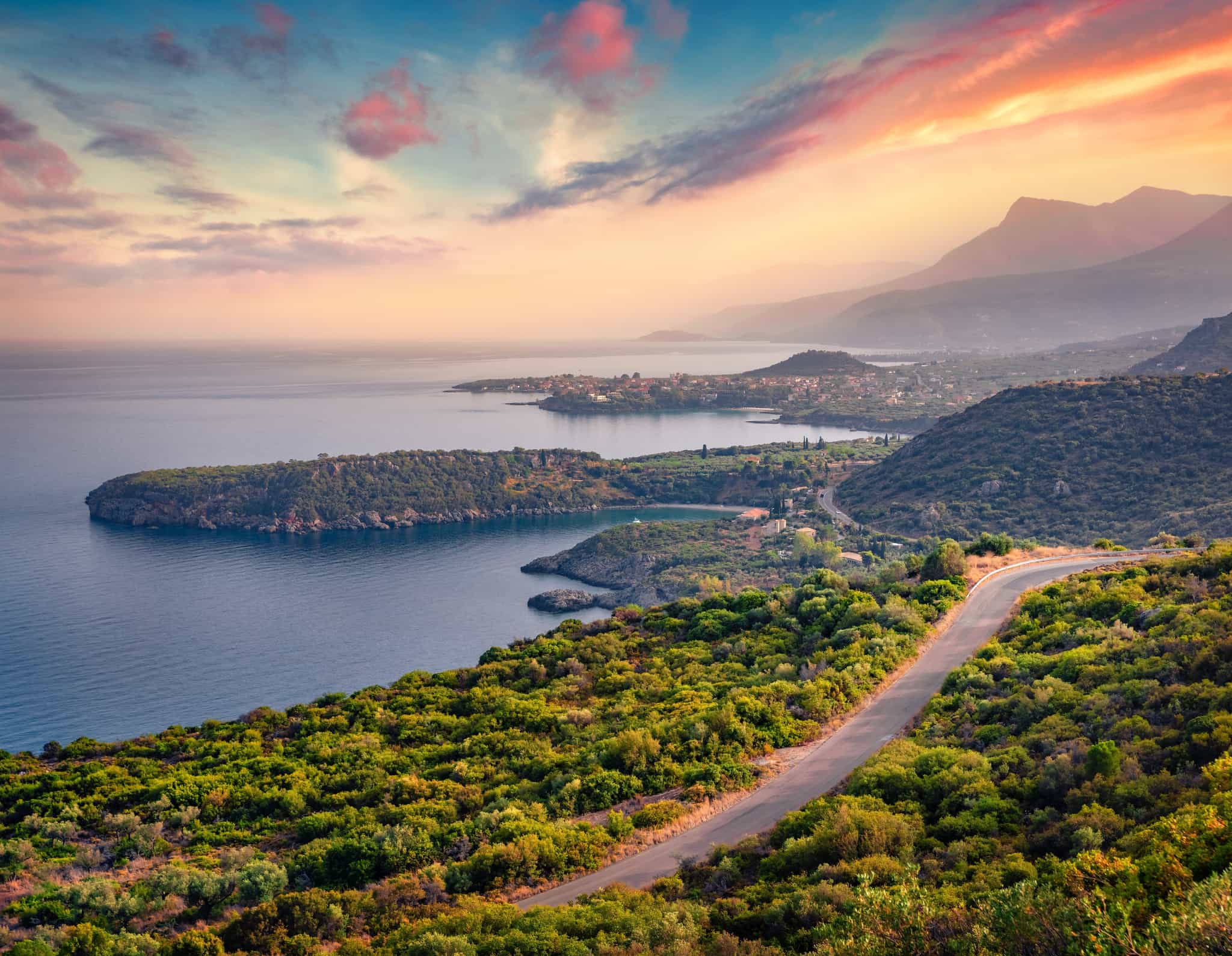 Road winds along the coast at sunset in the Peloponnese, Greece.